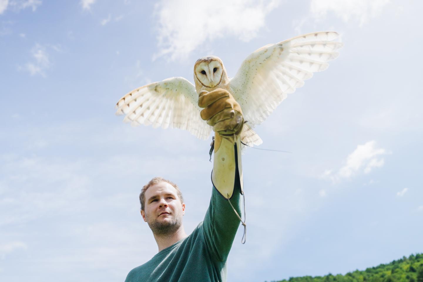 Man Holding Owl in Front of Cloudy Sky